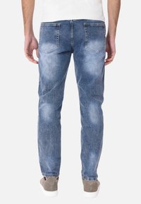 Jeans in denim azzurro chiaro con taglio dritto, dotati di due tasche posteriori e sottili sfumature di usura. Indossati con sneaker grigie.