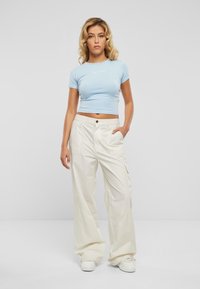 Lyseblå crop-top med korte ermer og hvit logo, kombinert med løstsittende, kremfargede cargo-bukser og hvite sneakers.