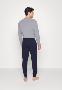 Grå langermet topp kombinert med marineblå joggebukser. Toppens passform er tettsittende med rund hals; buksene har elastiske mansjetter og snor i livet.