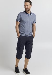 Menns polo skjorte i marin heather med hvite detaljer, kombinert med marineblå cargo shorts i kne-lengde med flere lommer og mørke joggesko.