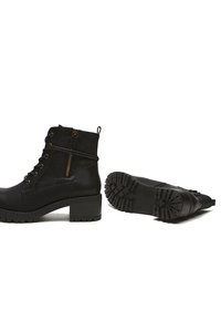 Botas negras hasta el tobillo con un tacón grueso, cordones en la parte delantera y cremallera lateral. Presentan una suela de goma con patrones de tracción. Acabado suave similar al cuero.