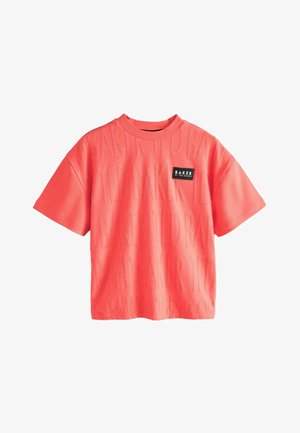 Korallenrotes T-Shirt mit kurzen Ärmeln aus weichem Stoff, das ein durch das gesamte Kleidungsstück geprägtes Logodesign und einen rechteckigen Logopatch auf der Vorderseite zeigt.