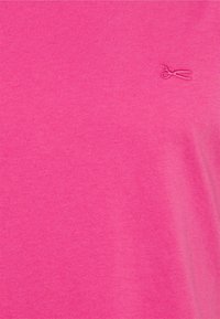 Maglietta rosa brillante in tessuto morbido. Presenta un piccolo logo ricamato a forma di forbici sul lato sinistro. Design semplice e aderente.