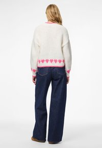 Λευκό πλεκτό πουλόβερ με ροζ μοτίβο καρδιάς στο τελείωμα και στις μανσέτες, συνδυασμένο με τζιν παντελόνι φαρδιάς εφαρμογής. Μαλακή υφή, άνετη γραμμή.