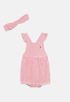 Combinaison pour bébé rayée rouge et blanche avec bretelles à volants et bandeau assorti noué, sur fond blanc.