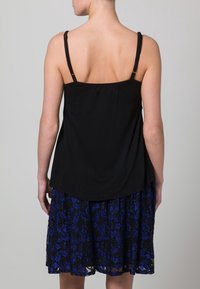 Top negro sin mangas con tirantes delgados, combinado con una falda de encaje azul y negra que presenta patrones florales y un diseño acampanado.