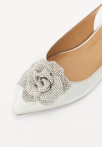 Weißes Leder Schuh mit spitzem Zehenbereich, der auf der Vorderseite mit einer strukturierten silbernen Strass-Rosenverzierung versehen ist, und einem glatten Innenfutter.