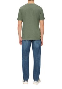 Oliwkowa bawełniana koszulka z krótkim rękawem, okrągłym dekoltem i luźnym krojem, zestawiona z niebieskimi jeansami w wąskim kroju. Prosty design, bez wzorów.