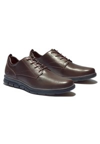 Chaussures décontractées pour hommes en cuir marron avec lacets, semelles en caoutchouc noir, petit talon et détails de couture subtils, placées côte à côte sur fond blanc.