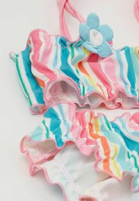 Maillot de bain rayé coloré avec des bords volants, principalement en rose, bleu et orange. Présente un accent floral bleu sur le haut.