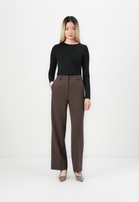 Črna dolgosleeve majica v kombinaciji z visokim pasom, rjavimi širokimi hlačami, ki imajo gladko teksturo in minimalističen dizajn.