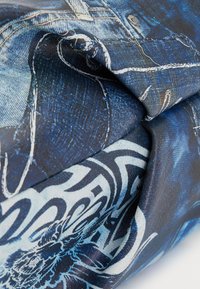 Blue denim fabric featuring intricate patterns. The material has a textured finish with a mix of darker and lighter blue tones.