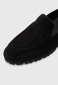 Svart semsket slip-on sko med rund tå, fremtredende søm og teksturert gummisåle for godt grep. Elastiske detaljer på sidene.