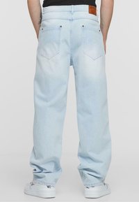 Light blue denim pants with a relaxed fit, featuring a leather patch, back pockets, and subtle fading. Paired with white shoes.