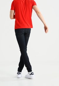 Camiseta roja de manga corta, jeans oscuros y zapatillas blancas con acentos negros. Los jeans son ajustados, con una textura suave y detalles mínimos.