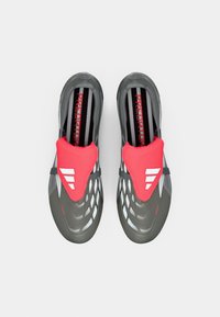 Zapatos deportivos con parte superior de malla gris y acentos en rojo brillante, diseño aerodinámico, plantilla texturizada y el icónico logo de tres rayas.