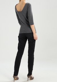 Grauer eng anliegender Oberteil mit weitem Rund-Ausschnitt und Dreiviertelärmeln, kombiniert mit schwarzen schmal geschnittenen Hosen und grauen High Heels. Glatte Textur über die gesamte Fläche.