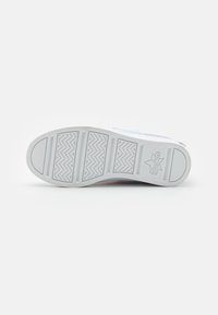 Suela de zapatilla blanca con patrón de tracción en zigzag y el logo "Skechers" grabado cerca del talón, vista desde la parte inferior sobre un fondo blanco.