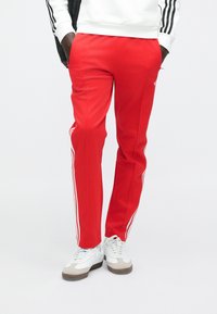 Červené teplákové kalhoty z hladké látky s bílými postranními pruhy a elastickým pasem. Doplněné o sladěné tenisky.