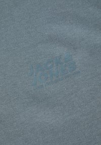 Grijze katoenen T-shirt met een verhoogde, ton-on-ton bedrukking van "JACK & JONES" met aanvullende tekst eronder. Zachte textuur, casual ontwerp.