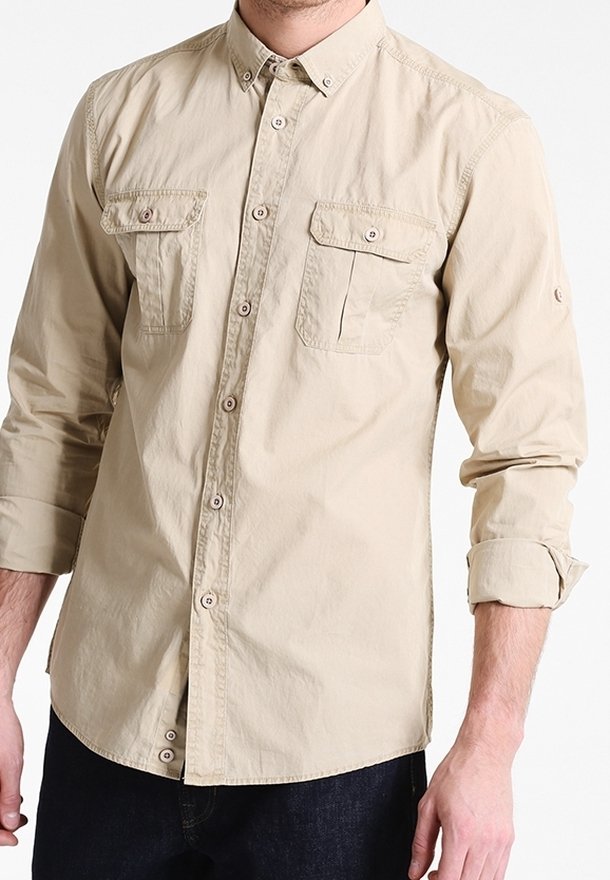 Camicia beige con colletto, due tasche sul petto, maniche arrotolate e bottoni marroni. Il tessuto è liscio con una leggera texture.