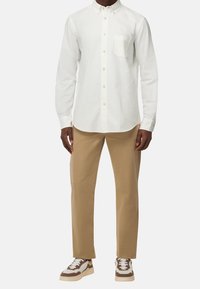 Vit långärmad skjorta med knappar och bröstficka, parat med beige chinos och bruna/vita sneakers. Slät tyg, skräddarsydd passform.