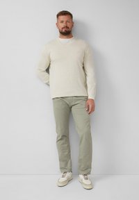 Lichtbeige V-hals trui en lichtgroene slim-fit broek, gecombineerd met witte sneakers. Eenvoudig ontwerp, zachte textuur en neutrale kleuren.