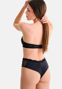 Ensemble de lingerie noire comprenant un soutien-gorge rembourré avec bordure en dentelle et des culottes taille haute avec des panneaux latéraux transparents à pois.