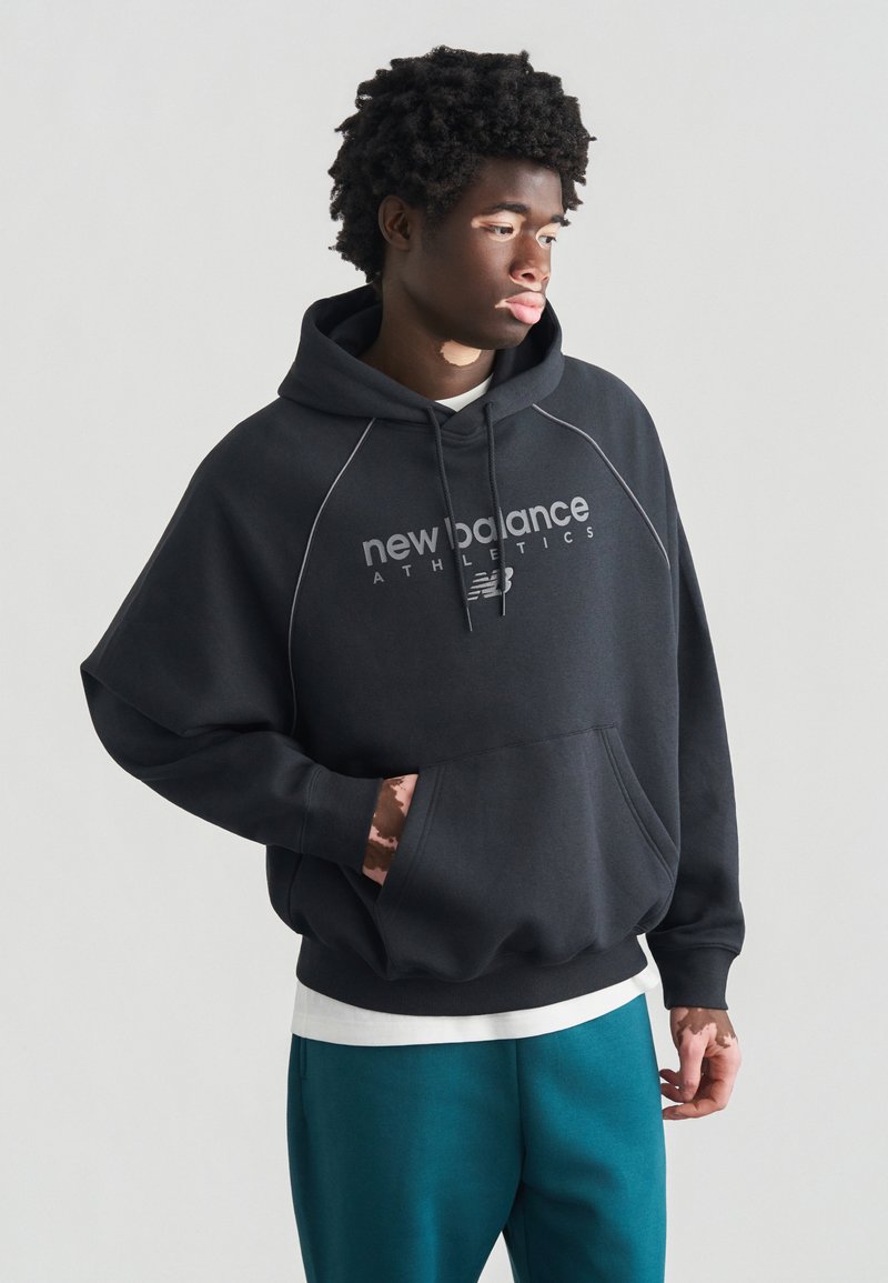 Zwart hooded sweatshirt met voorvak, voorzien van een witte logotekst "new balance athletics" en grijze accenten, gedragen over een wit shirt.