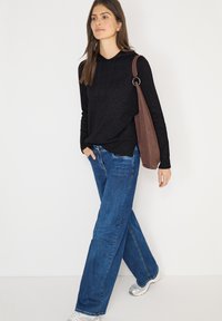 Zwarte hoodie met een gestructureerde afwerking, gecombineerd met blauwe wijde jeans en zilveren sneakers. Bruine schoudertas met een ronde handgreep.