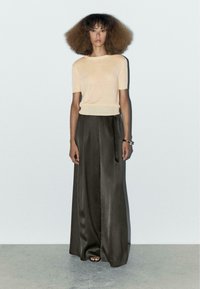 Korte mouw perzikkleurige gebreide top, gecombineerd met donkergrijze, wijde satijnen broeken. Zachte textuur met een ontspannen pasvorm en een gladde afwerking.