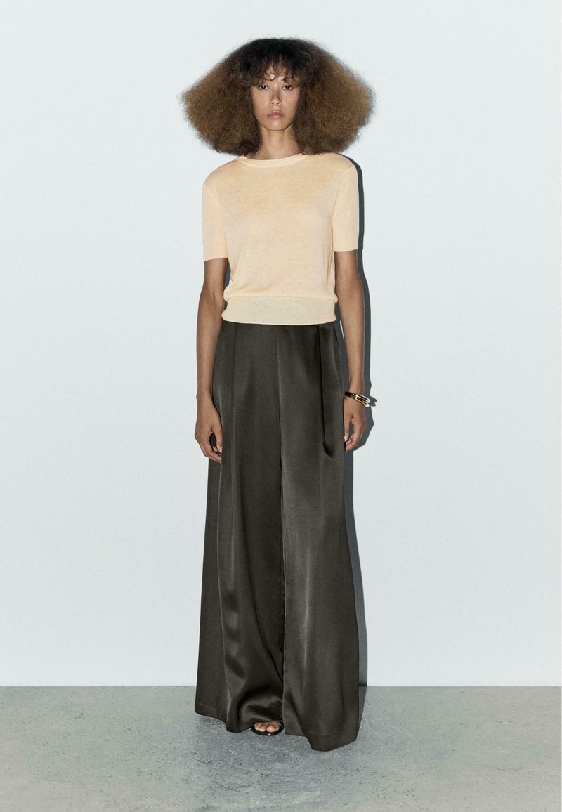 Korte mouw perzikkleurige gebreide top, gecombineerd met donkergrijze, wijde satijnen broeken. Zachte textuur met een ontspannen pasvorm en een gladde afwerking.