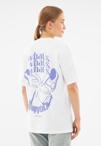 Biała bawełniana koszulka z dużym fioletowym motylem na grafikę z tekstem z tyłu. Luźny krój, krótkie rękawy i okrągły dekolt.