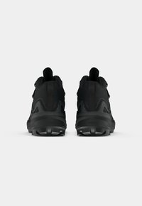 Ein Paar schwarze Sportschuhe mit robusten Sohlen, von hinten auf einem schlichten weißen Hintergrund gezeigt.