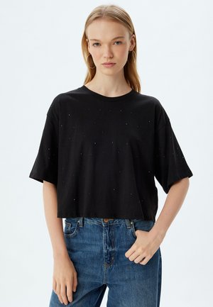 Zwarte cropped t-shirt van katoen, met een ronde halslijn en korte mouwen, versierd met kleine pailletten voor textuur. Gecombineerd met blauwe jeans.
