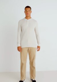 Lys beige langermet skjorte med knappestolpe, kombinert med brune bukser og svarte sko. Glatt tekstur, skreddersydd passform. Minimalistisk design.