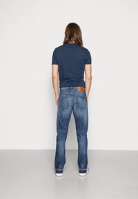 Navy blue t-shirt paired with faded blue jeans. Denim has a visible leather patch and two back pockets, with a casual sneaker design.