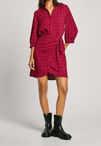 Vestido Camisero de estampado rojo con mangas tres cuartos y cintura ajustada. Combinado con botas negras hasta el tobillo con suela gruesa.