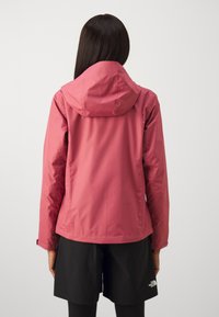 Pink waterproof jacket with a hood, smooth texture, adjustable cuffs, and a cinched waist. Worn over black shorts.
