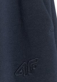 Tissu tricoté bleu foncé avec un logo 4F en relief brodé près du coin inférieur droit.