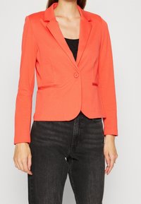 Blazer corail à la coupe ajustée, fermeture à un bouton et deux poches avant. Confectionné dans un tissu lisse et extensible. Manches longues.