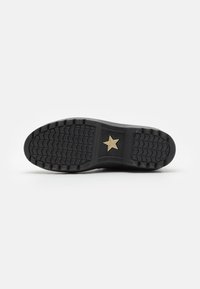 Suela de zapato de goma negra con un patrón de textura y un acento en forma de estrella dorada. Bordes suaves, construcción duradera y un diseño funcional.
