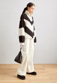 Suéter de punto de gran tamaño en blanco y negro con patrón de zigzag, con un cuello alto, combinado con pantalones de pierna ancha crema y zapatos de plataforma negros chunky.