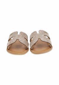 Rose gold slip-on sandals with a textured upper, cutout design, and a flat tan outsole. Features metallic accents on the straps.