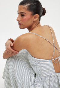 Robe rayée avec une silhouette fluide, dotée de fines bretelles croisées et d'un dos ouvert. Les couleurs comprennent des rayures blanches et bleues.