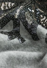 Tissu de pull gris orné d'un motif noir en sequins avec des motifs complexes, mettant en valeur une surface texturée et des embellissements détaillés.