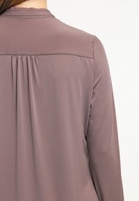 Langärmliges Oberteil aus weichem, sanften Mauve-Stoff. Verfügt über ein Faltendetail unter dem Schulterbereich, das eine drapierte Rückensilhouette erzeugt.