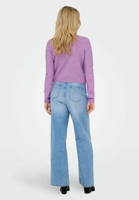 Ljuslila tröja med långa ärmar, matchad med högmidjade, löst sittande ljusblå jeans. Svarta klackstövlar med synliga sömdetaljer.