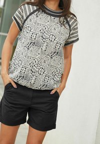 Haut à manches courtes à motifs crème avec des dessins géométriques noirs ; associé à un short noir retroussé. Le tissu semble doux et décontracté.