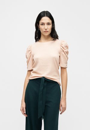 Lyserød tekstureret top med pufærmer, parret med højttaljede mørkegrønne bukser med et bundet bælte. Minimalistisk design.